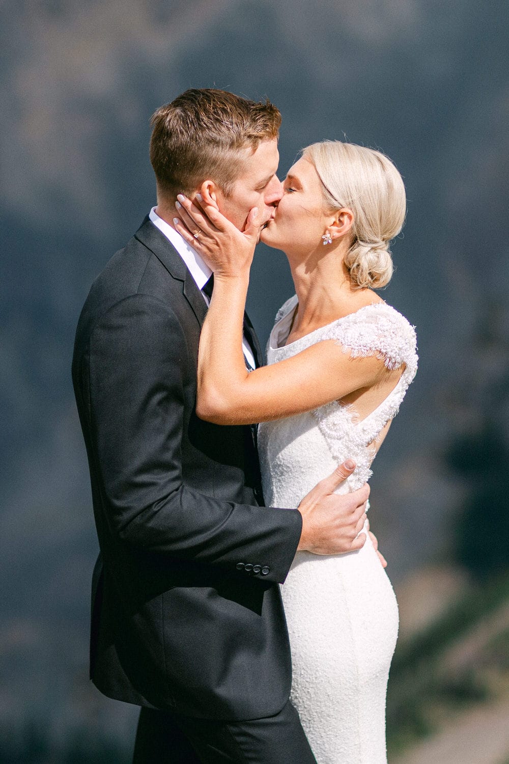 A bride and groom share a kiss, surrounded by a scenic backdrop, capturing the essence of love and celebration on their special day.