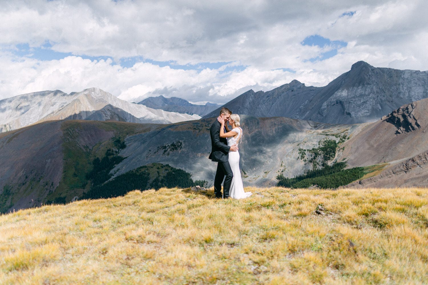 A couple embraces in a romantic pose amidst stunning mountain scenery, capturing a moment of love and nature.