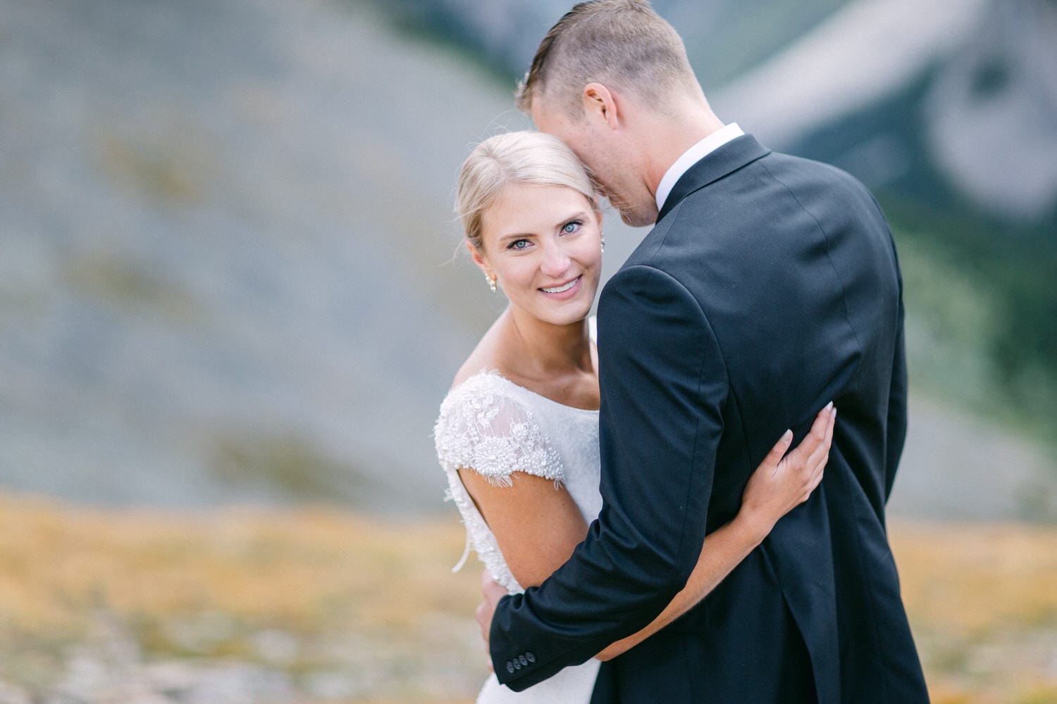 A bride and groom embrace in a serene outdoor setting, capturing a joyful and romantic moment together.