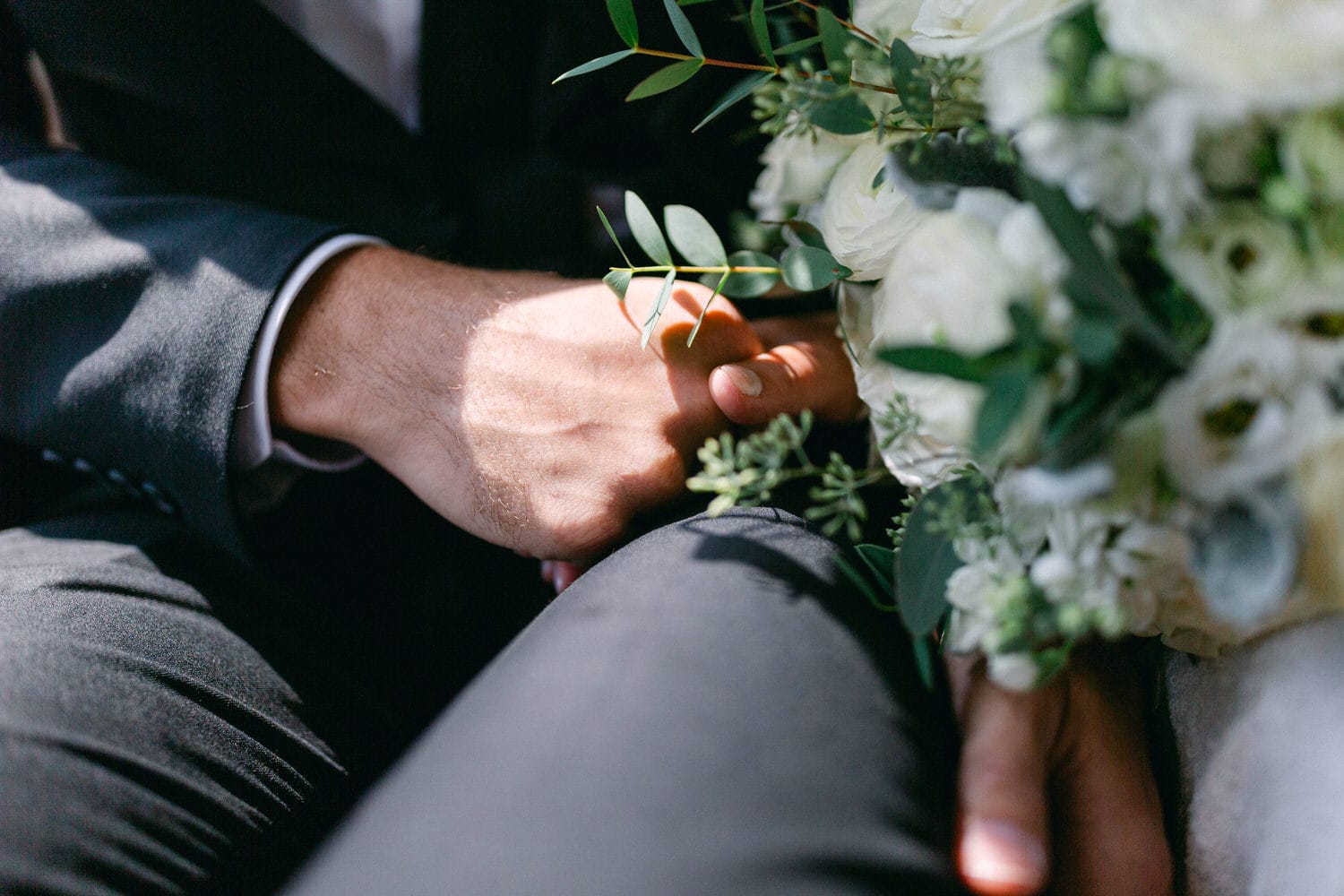 Close-up of hands holding each other with a bouquet, symbolizing love and connection.