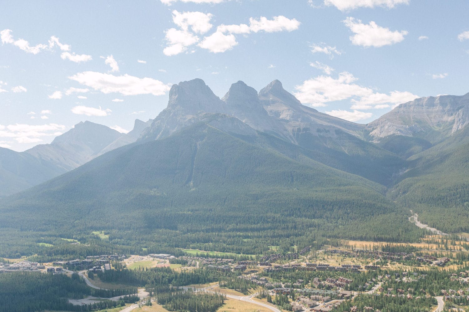 A panoramic view of rugged mountains towering over a lush green valley, with a small town nestled at the base.