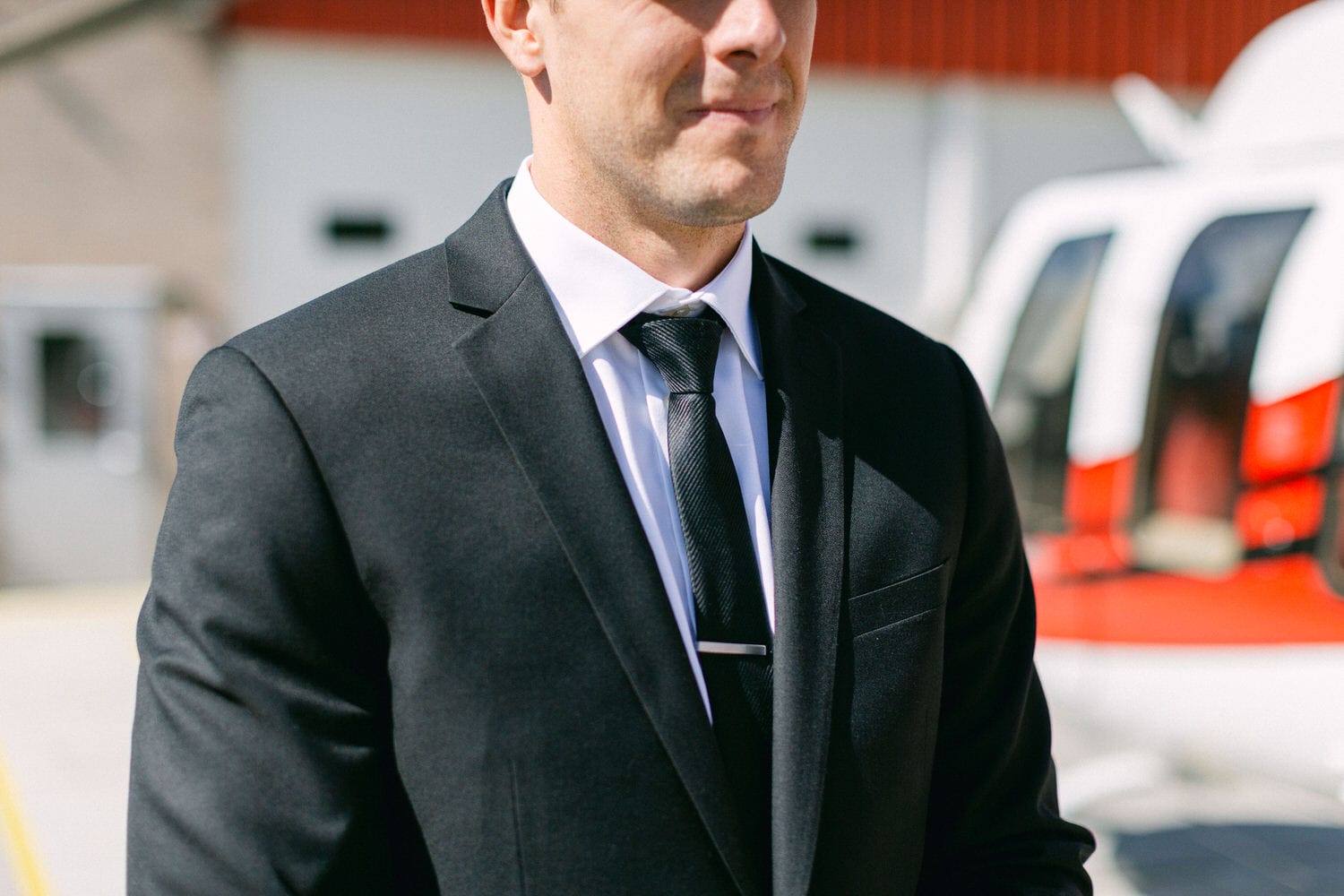 A well-dressed man in a suit and tie stands in front of a helicopter, showcasing a blend of elegance and adventure.