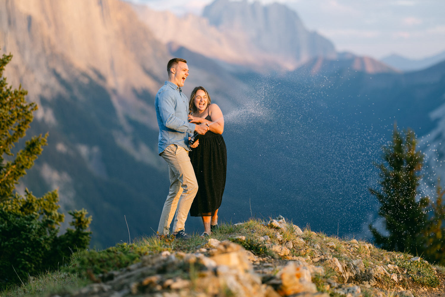 A couple joyfully spraying champagne on a scenic mountain backdrop, capturing a moment of happiness and adventure.