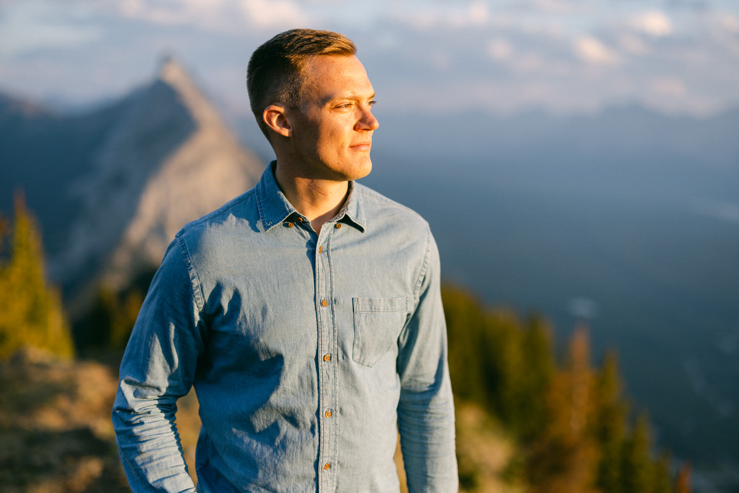 A man in a denim shirt stands in profile, gazing thoughtfully at a mountainous landscape bathed in golden light.