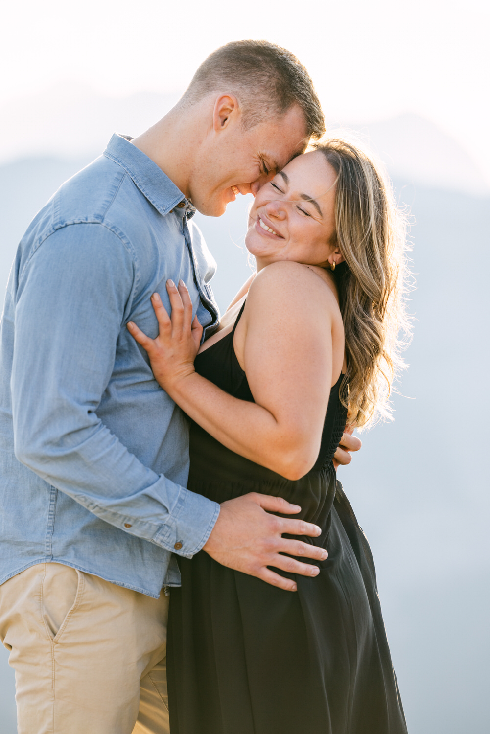 A joyful couple sharing an intimate moment outdoors, smiling while embracing, with a scenic background.