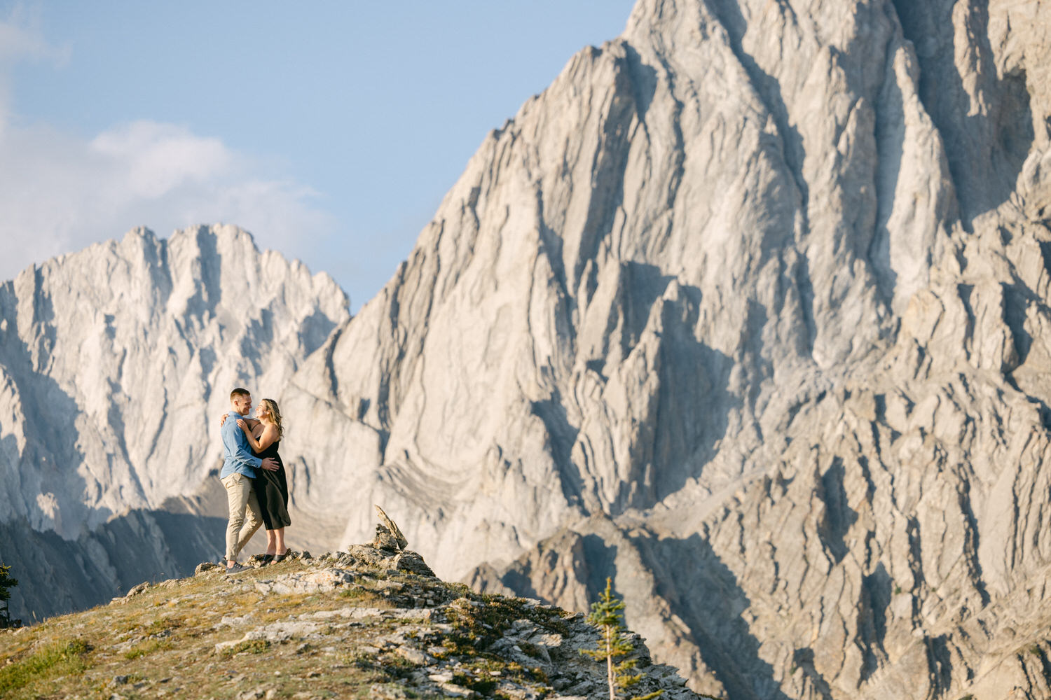 A couple shares an intimate moment on a rocky outcrop with majestic mountains in the background.