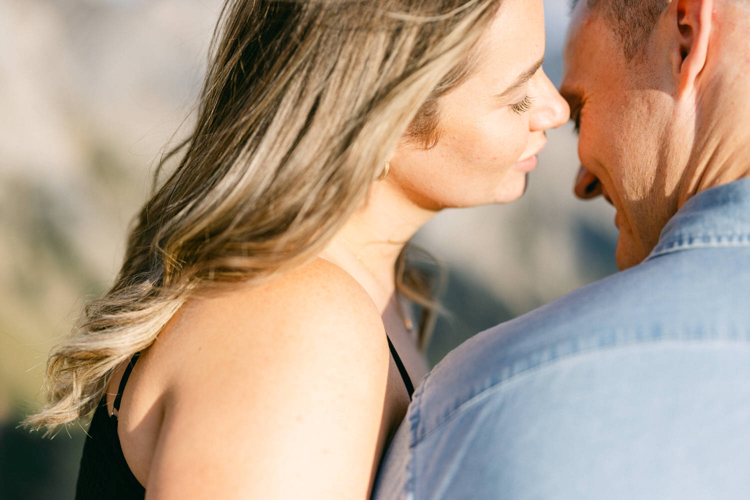 A close-up of a couple sharing an intimate moment, with their faces nearly touching, illuminated by soft sunlight.