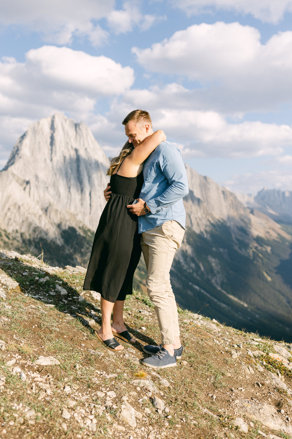 A couple shares a tender moment while embracing on a mountain backdrop, showcasing their love against a stunning natural landscape.