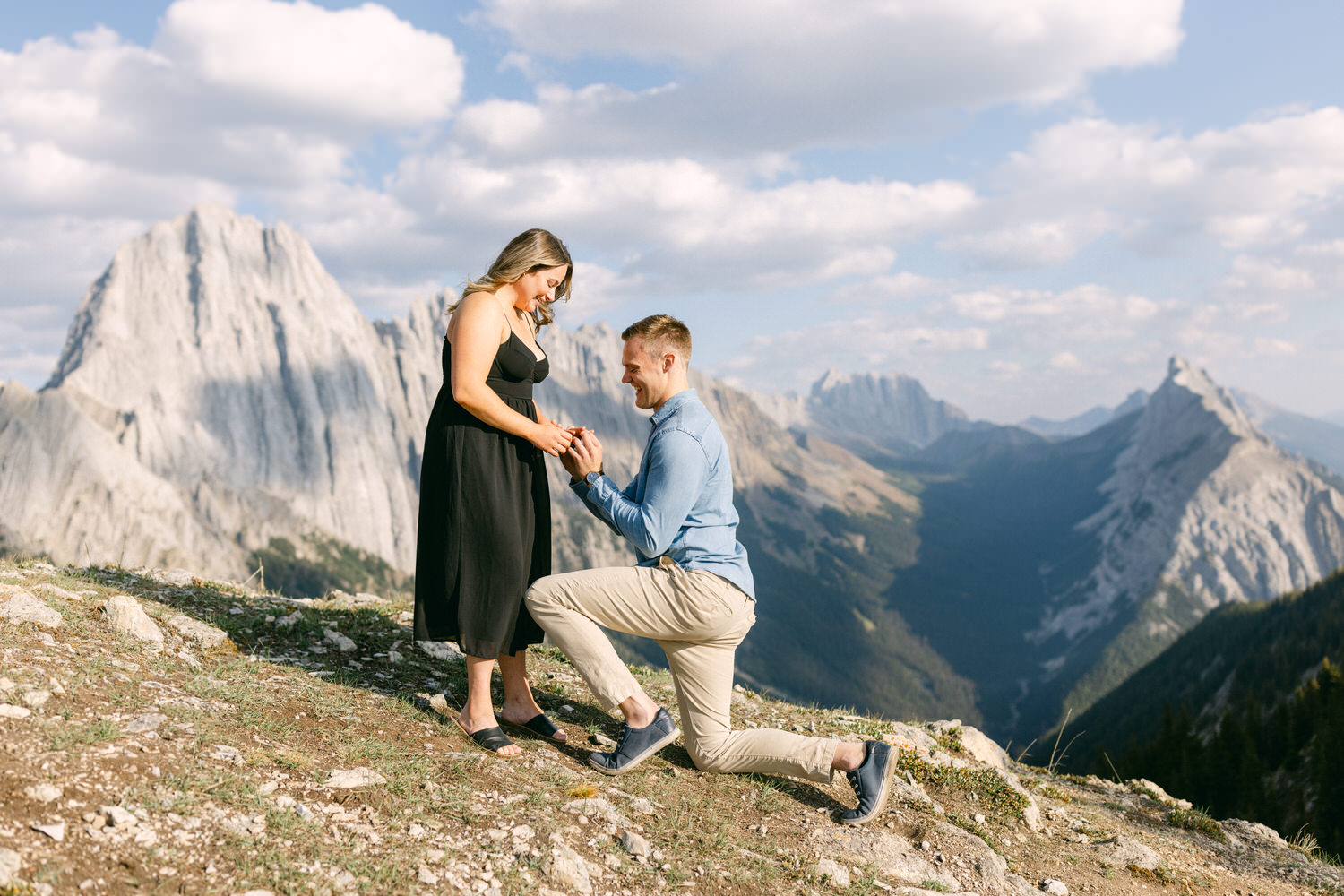 A man proposing to a woman with a stunning mountain backdrop, both smiling and engaged in a heartfelt moment.