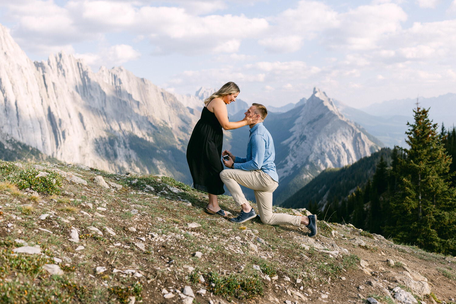 A couple enjoys a romantic proposal with breathtaking mountain scenery in the background, capturing a heartfelt embrace and a ring exchange.