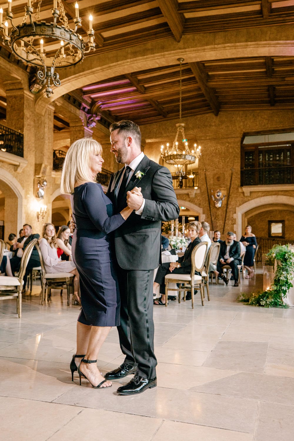 A couple elegantly dancing in a beautifully decorated venue, with guests seated in the background enjoying the moment.