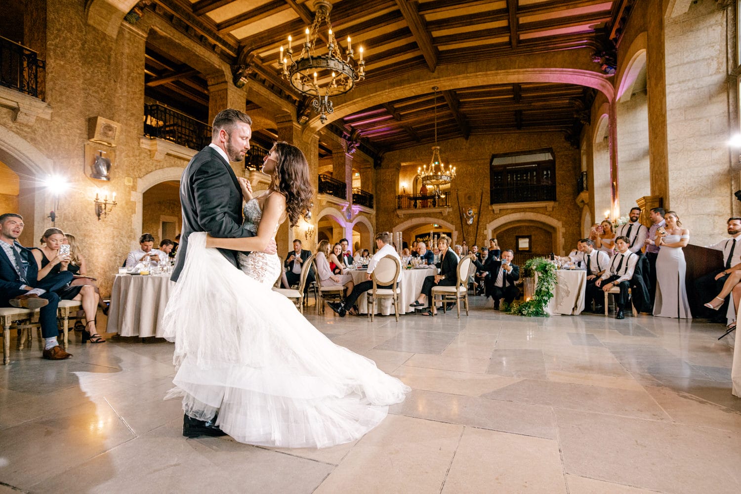 A couple shares an intimate first dance in a beautifully decorated banquet hall, surrounded by guests celebrating their special day.