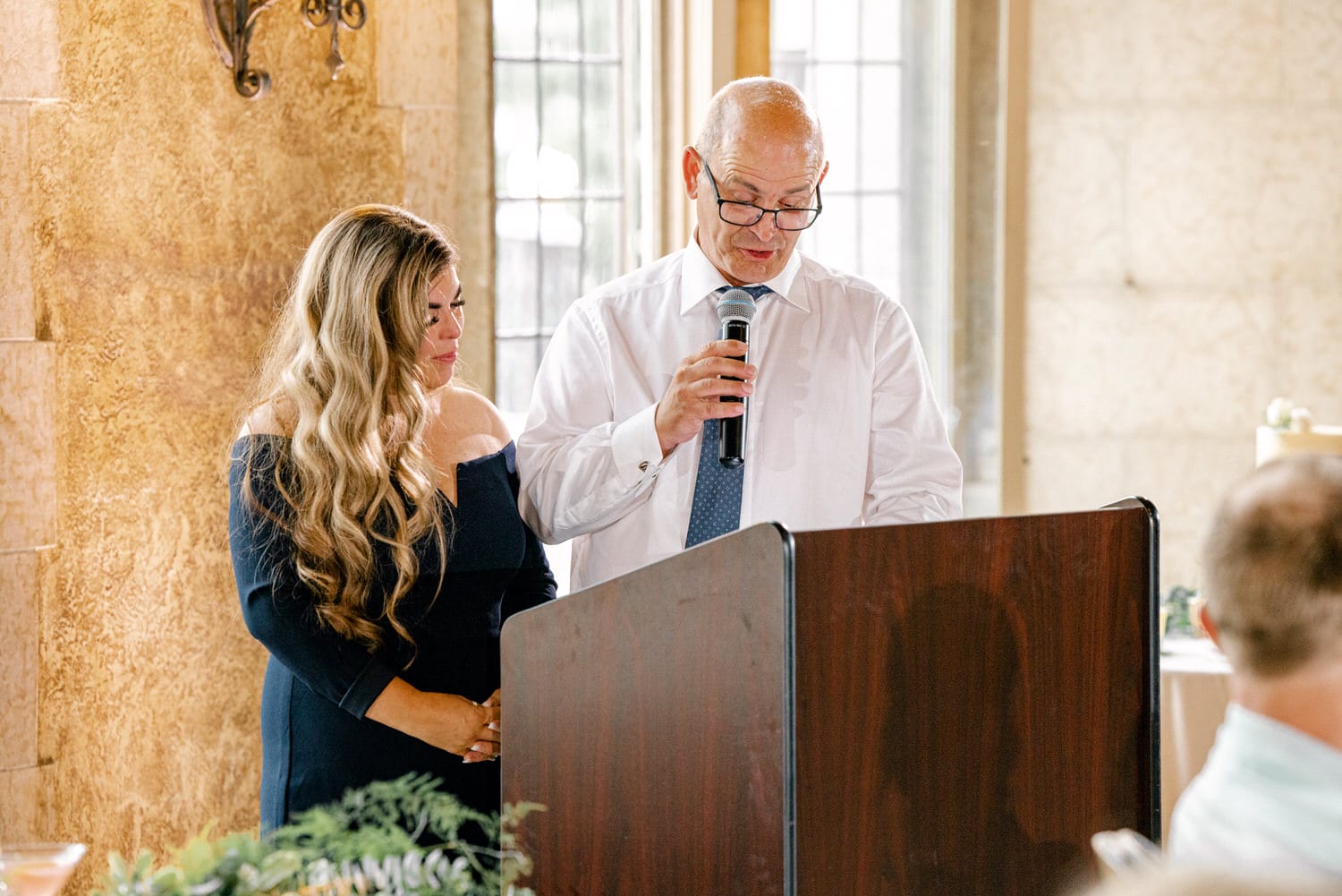 A man delivers a heartfelt speech while a woman listens attentively by his side during a special event.