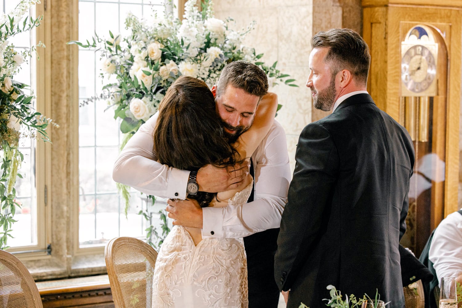 A joyful moment captured as a couple hugs amidst elegant floral arrangements, with guests smiling in the background.