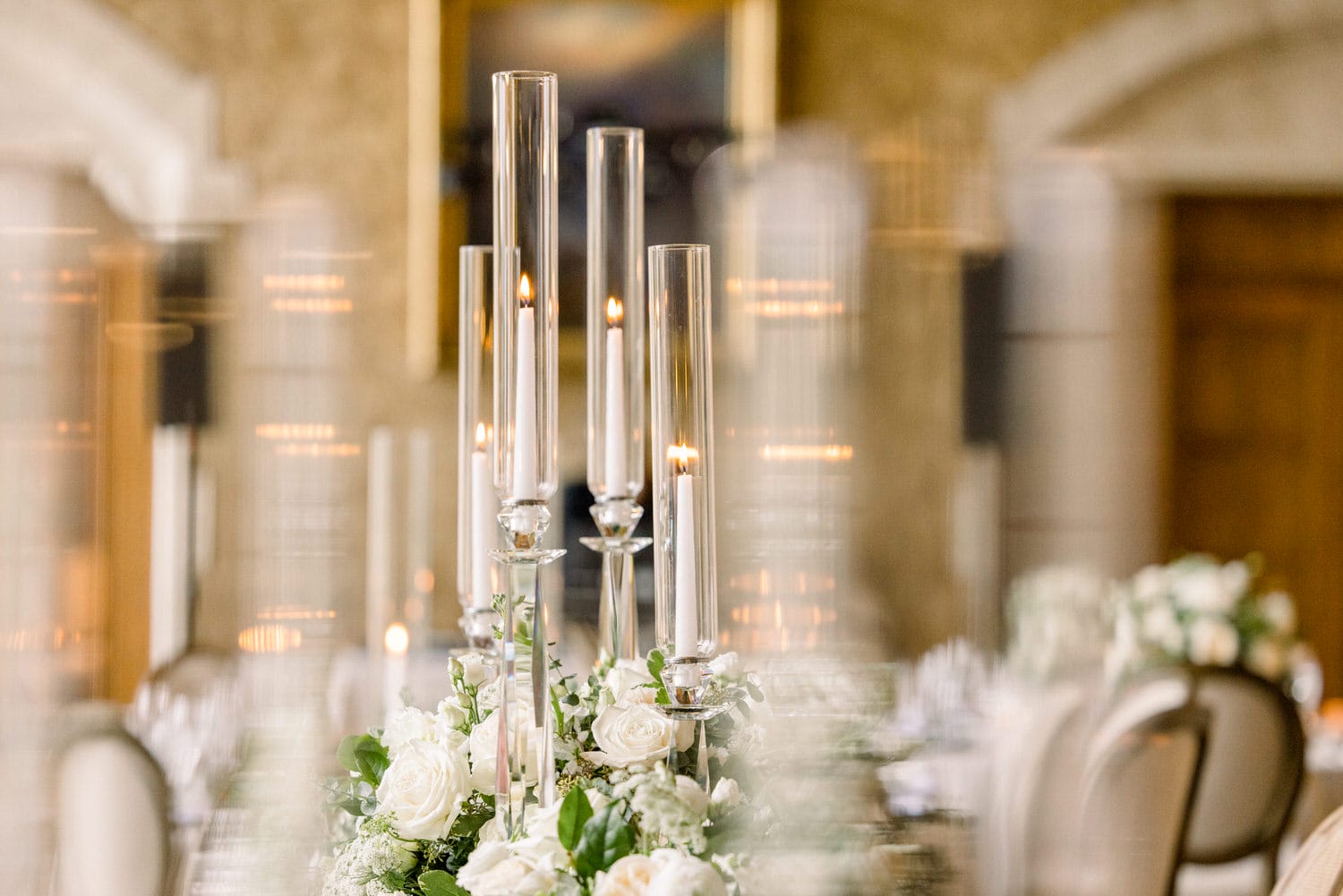 A beautifully arranged table featuring tall glass candle holders with flames, surrounded by white roses and greenery, creating a romantic ambiance.