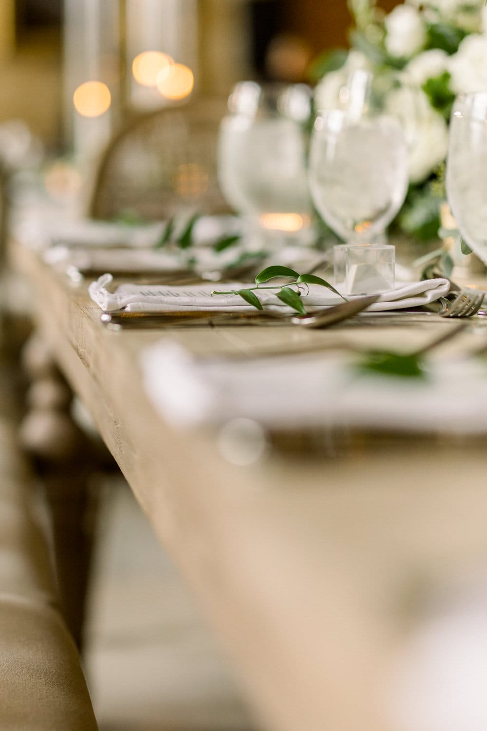 A beautifully arranged dining table featuring glassware, napkins, and greenery, set in a softly lit ambiance.