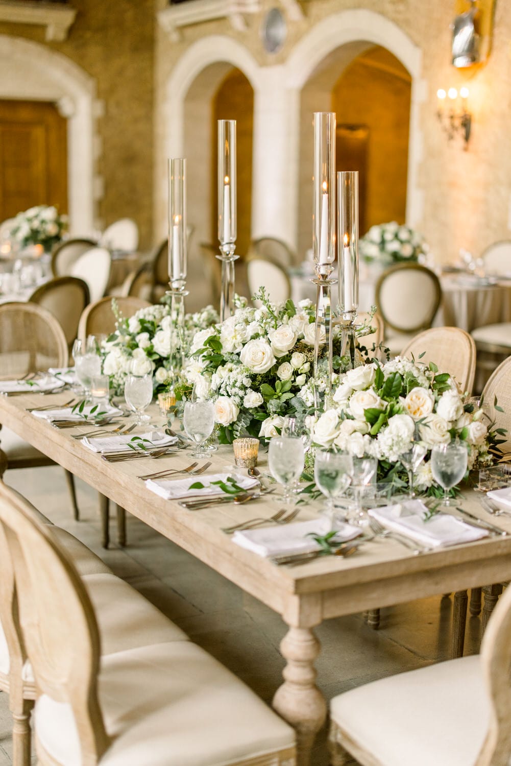 A beautifully arranged dining table with white roses, greenery, and tall candle holders set for a sophisticated event.