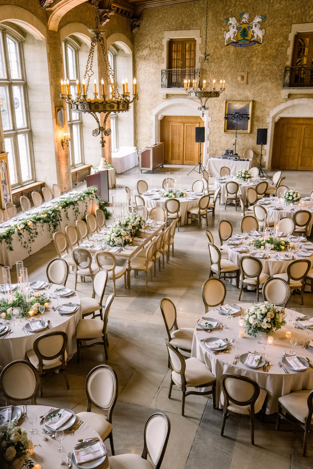 An elegantly decorated banquet hall with round tables, floral centerpieces, and chandeliers, ready for an event.