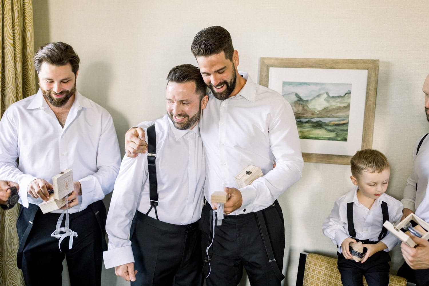 A group of groomsmen dressed in white shirts and black pants, smiling and sharing moments while preparing for a wedding, with one young boy in formal attire.