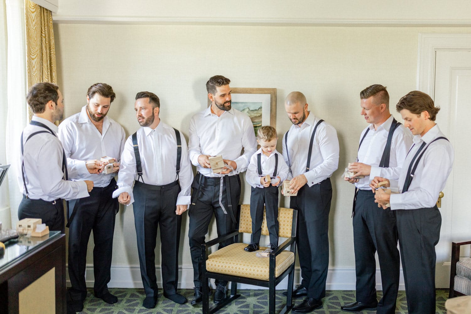 A group of well-dressed men, including a young boy, gathered in a room, holding small boxes and getting ready for a special occasion.