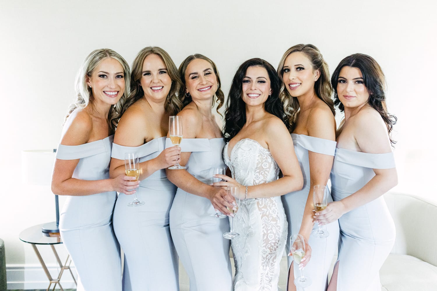 A joyful group of six women in elegant off-shoulder dresses, posing together with champagne glasses, celebrating a special occasion.