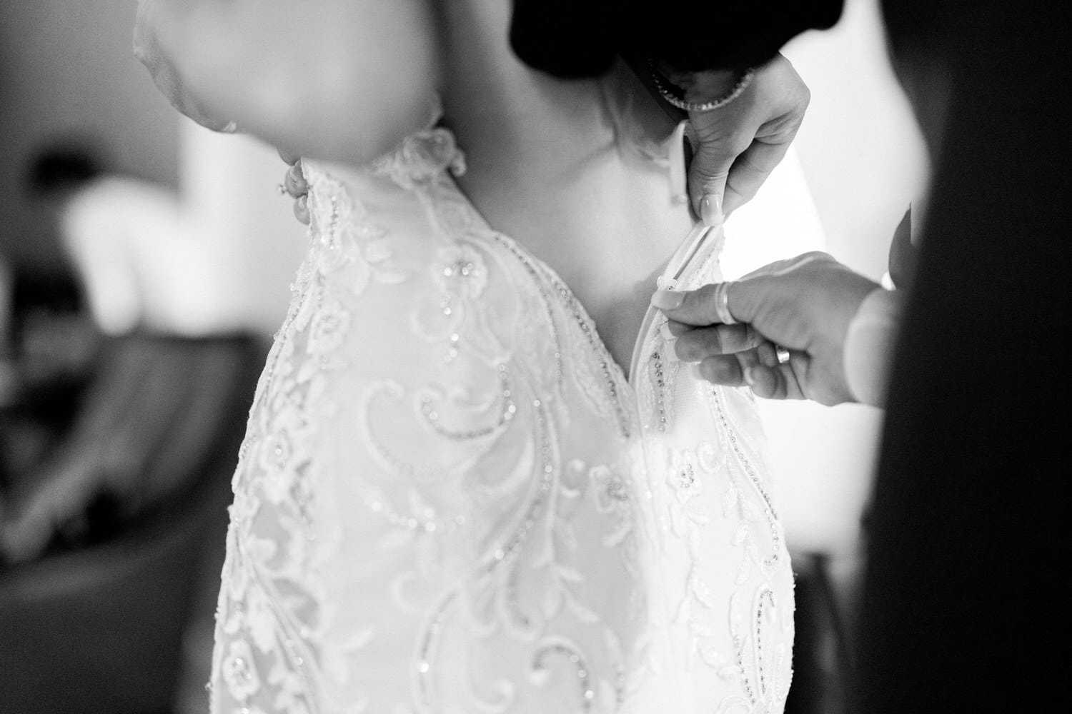 A close-up of hands fastening a wedding dress, highlighting intricate beading and elegant detailing.