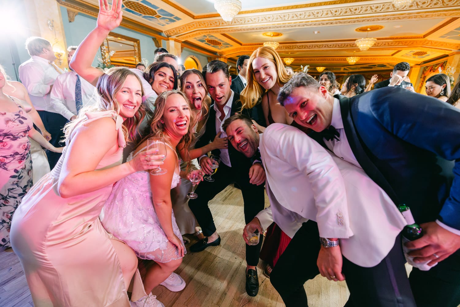 A lively group of people smiling and posing together at a vibrant celebration, with drinks in hand and a festive atmosphere.