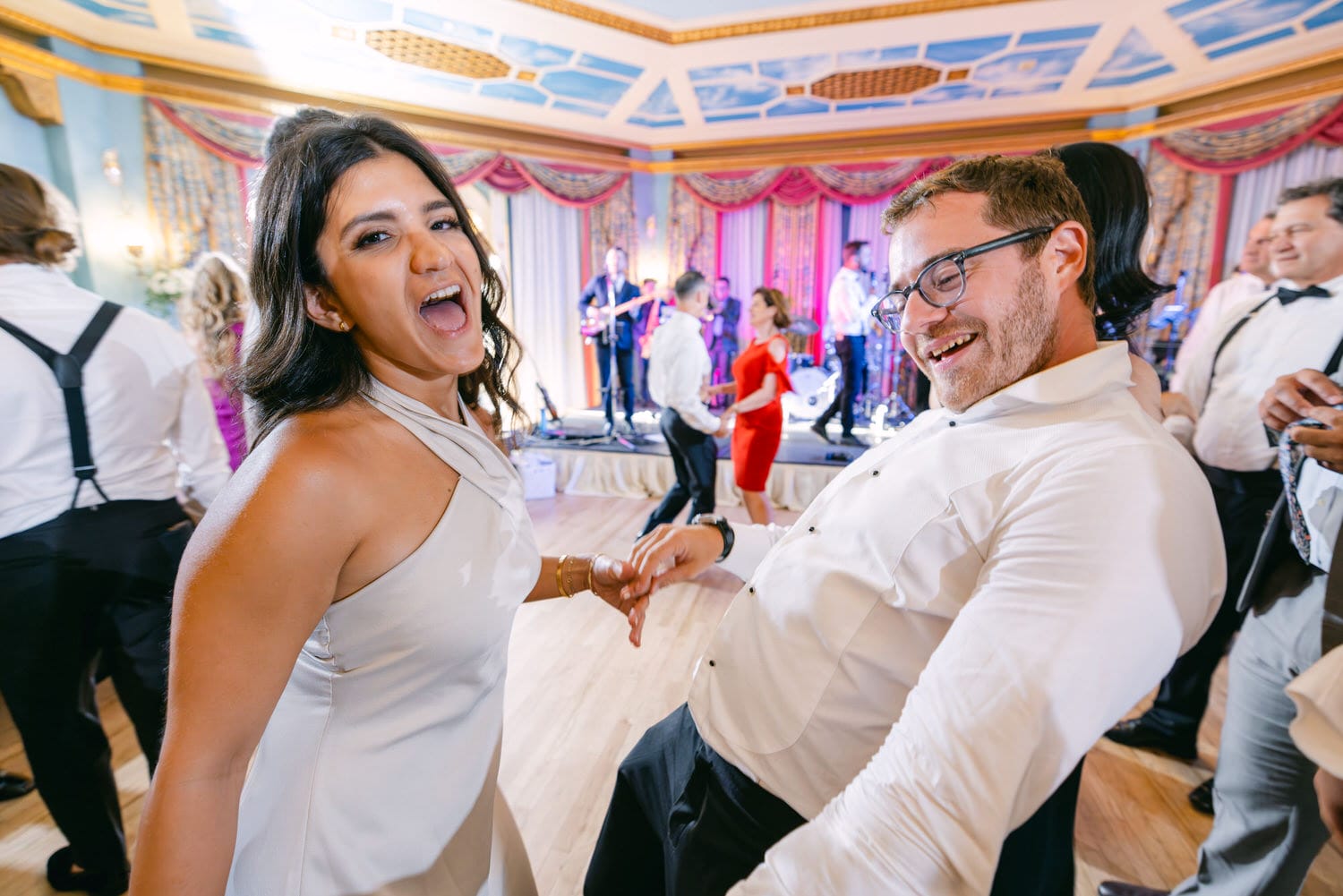 Two joyful guests enjoying a lively dance at a wedding reception, surrounded by others celebrating.