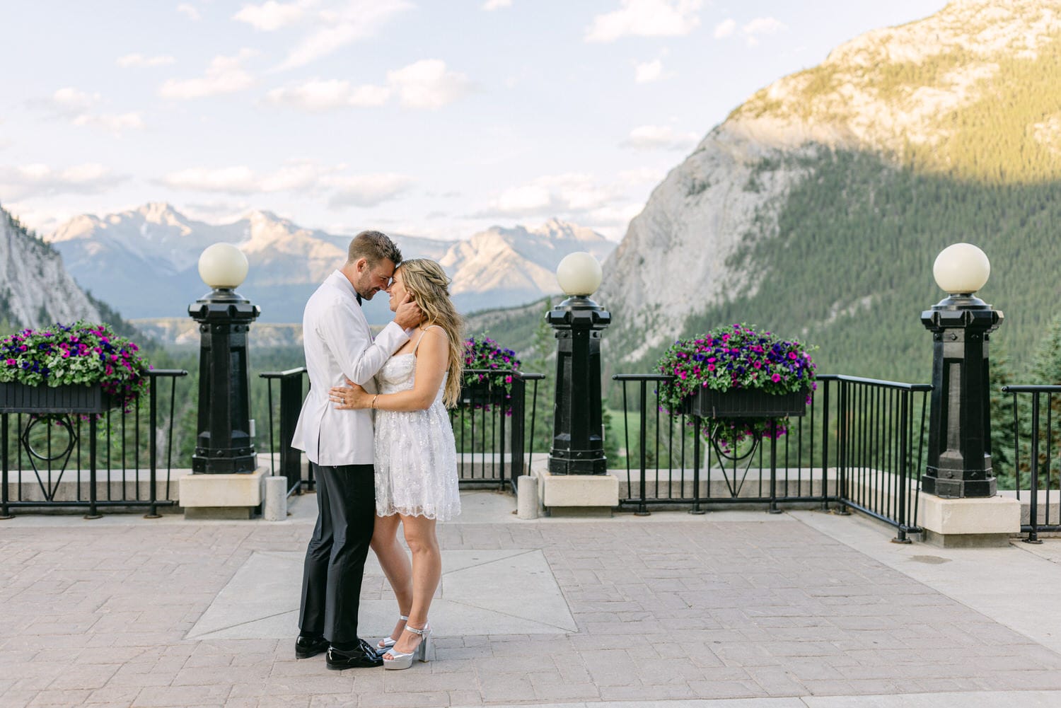 A couple sharing a tender moment on a scenic terrace with mountains in the background, surrounded by vibrant flower planters.