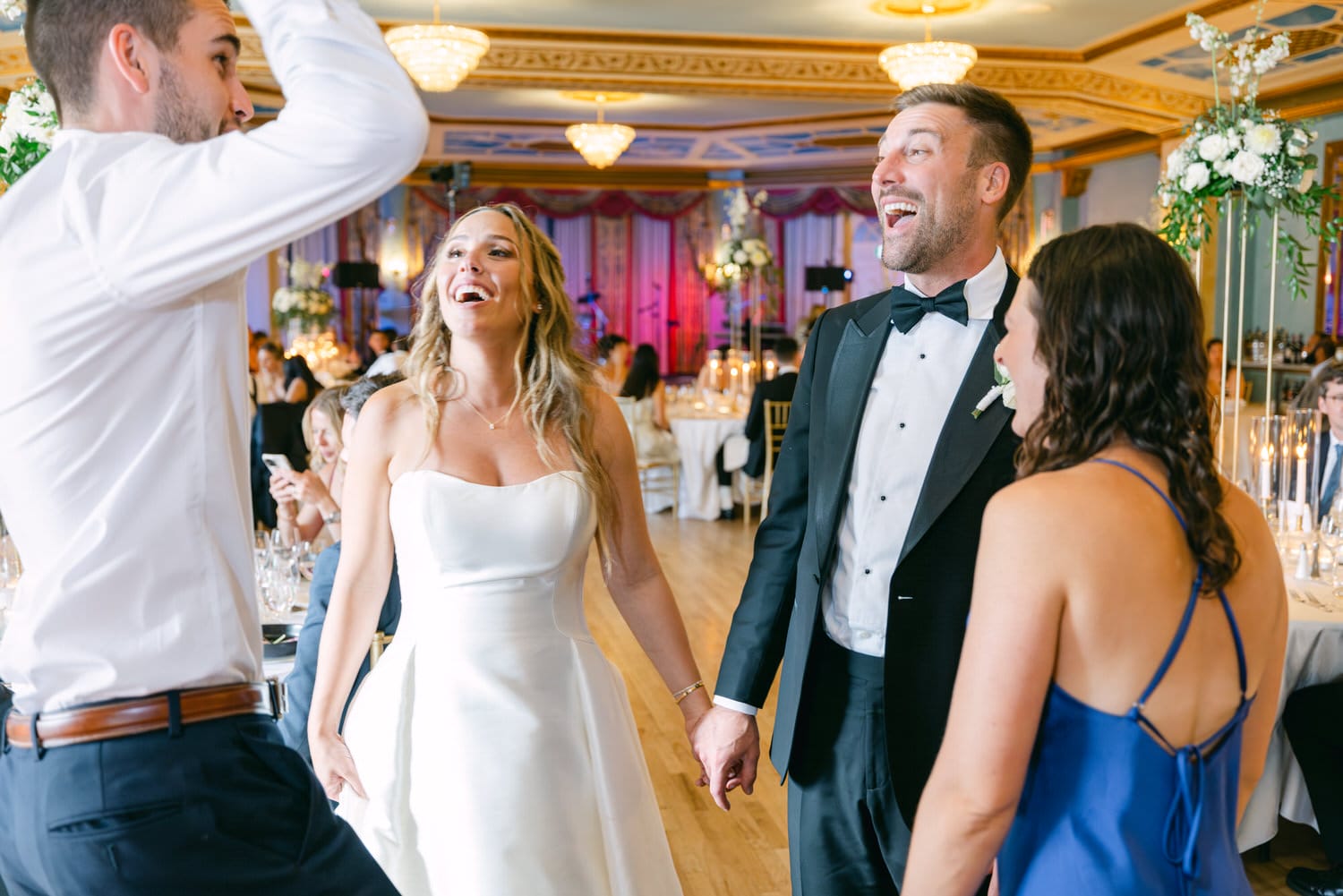 A bride laughing and dancing with friends during a lively wedding reception.