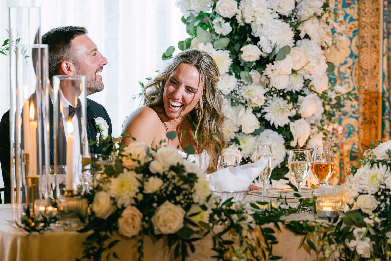 A couple shares a joyful moment during their wedding reception, surrounded by elegant floral arrangements and candles.