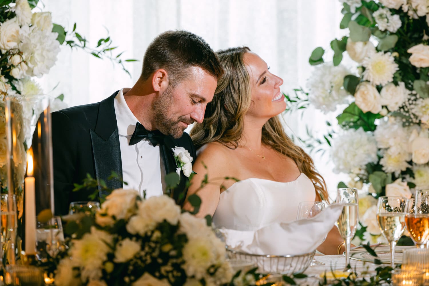 Couple sharing a joyful and intimate moment at their wedding reception, surrounded by elegant floral arrangements and candlelight.