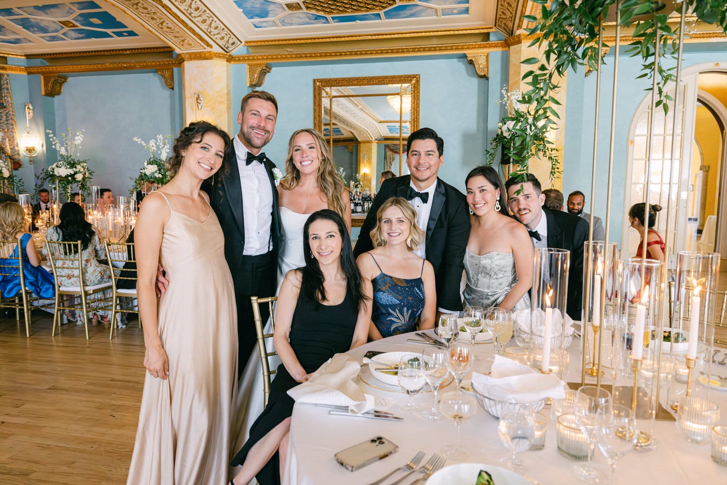 A cheerful group of friends posing together at a beautifully decorated table during a celebration in an elegant venue.