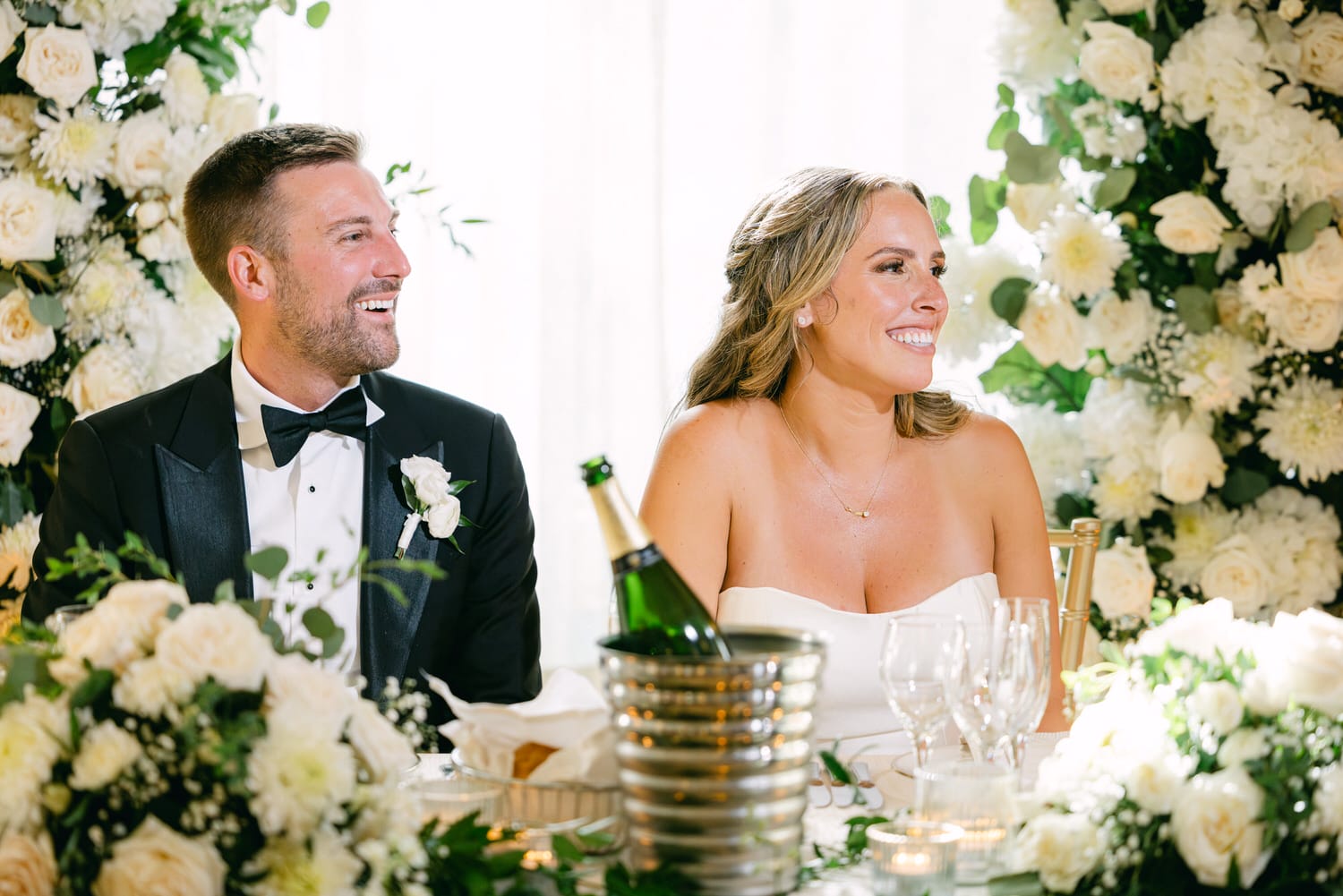 A couple sharing a joyful moment at their wedding reception, surrounded by elegant floral arrangements.