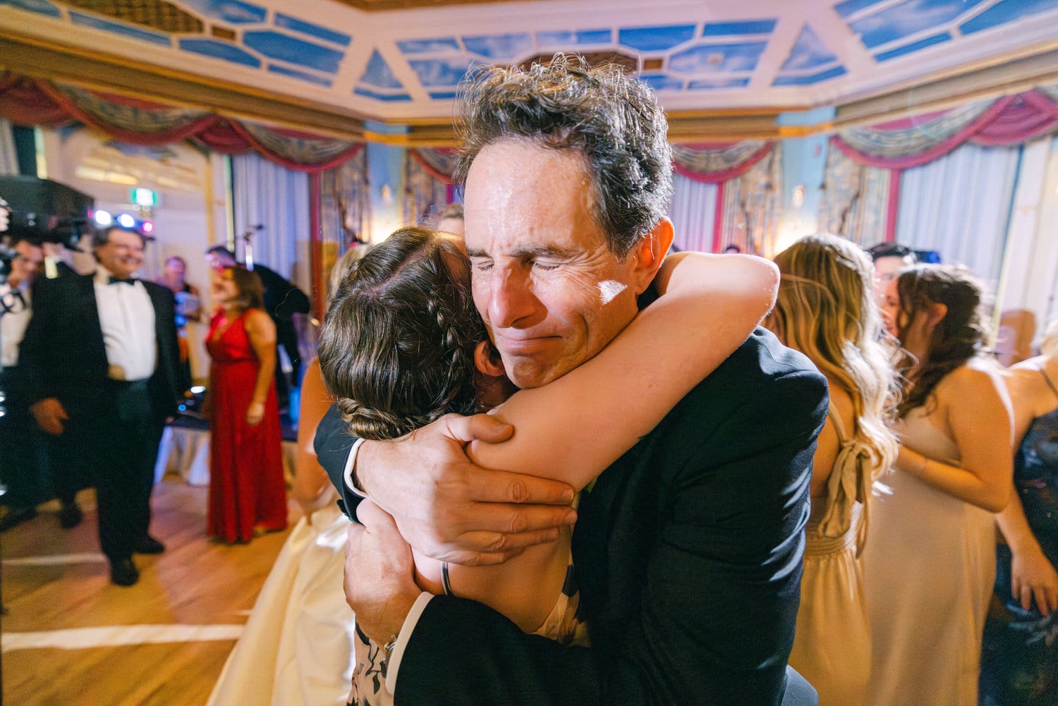 A heartfelt moment captured on the dance floor, featuring a man embracing a woman in joyful celebration amidst a lively gathering.