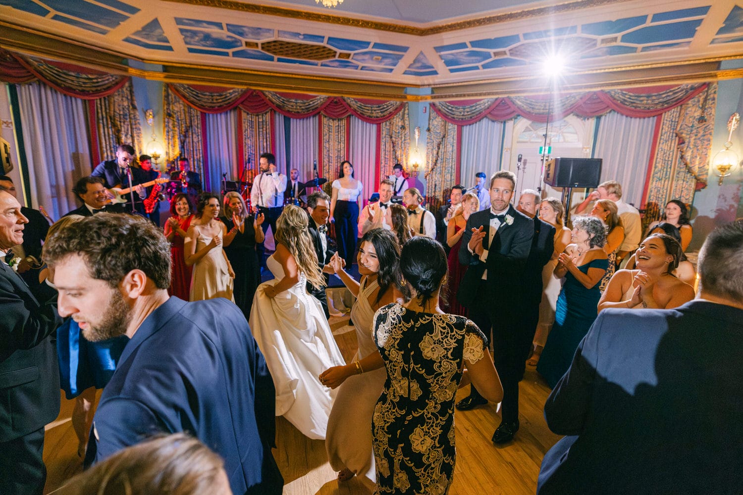 Guests dancing joyfully at a lively wedding reception with a band performing in the background.