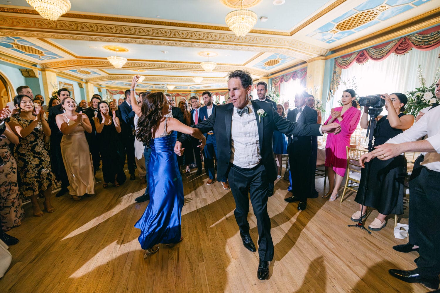 A lively scene of guests dancing joyfully at a wedding, dressed in elegant attire, with a beautiful venue and decorations in the background.