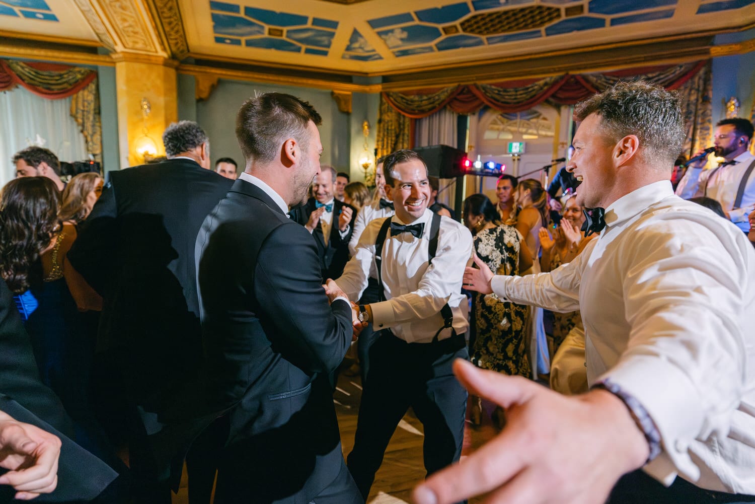 Group of men enjoying a lively celebration, laughing and dancing in a beautifully decorated venue.