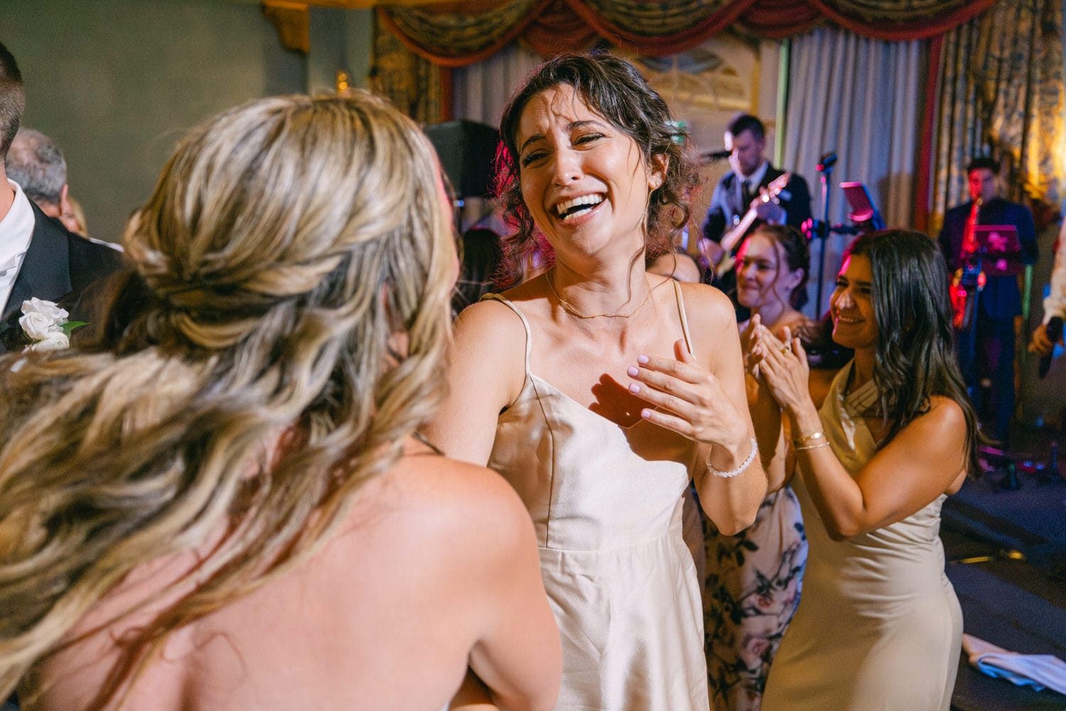 A group of women laughing and enjoying a lively celebration, with a band performing in the background.