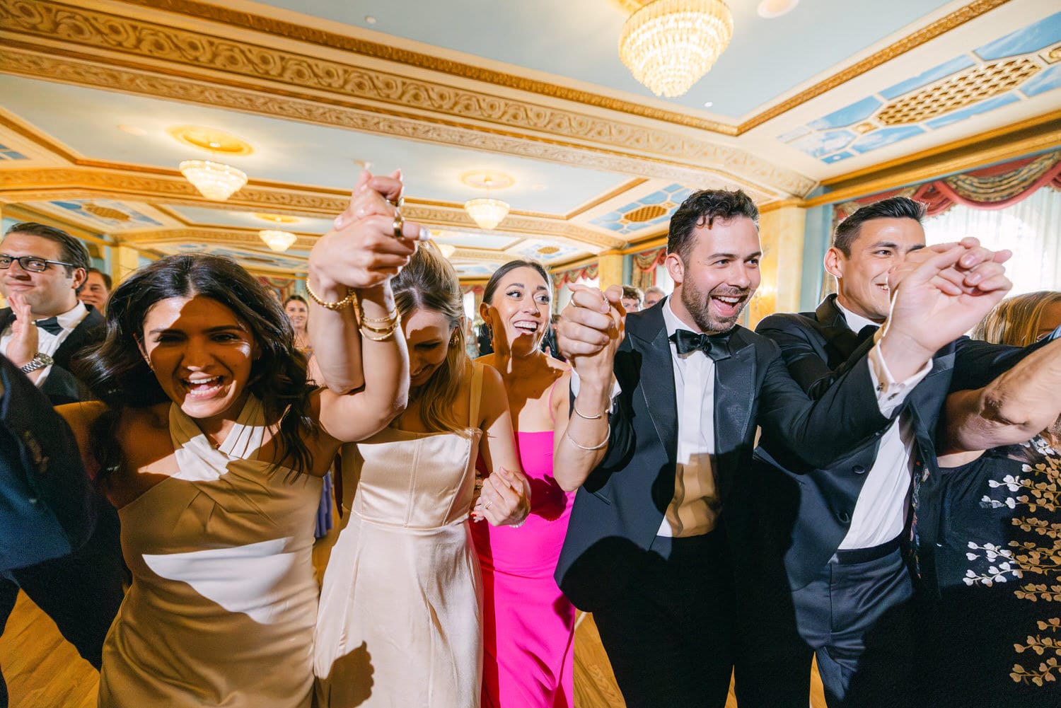 A joyful group dance at a wedding, showcasing guests holding hands and smiling in elegant attire.