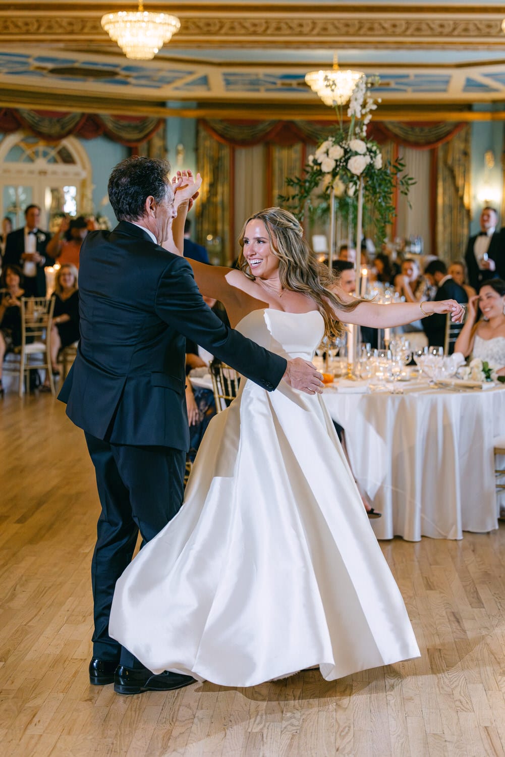 Joyful moment during a father-daughter dance at a wedding, showcasing the bride in a flowing white gown and her father dancing elegantly in a beautifully decorated reception hall.