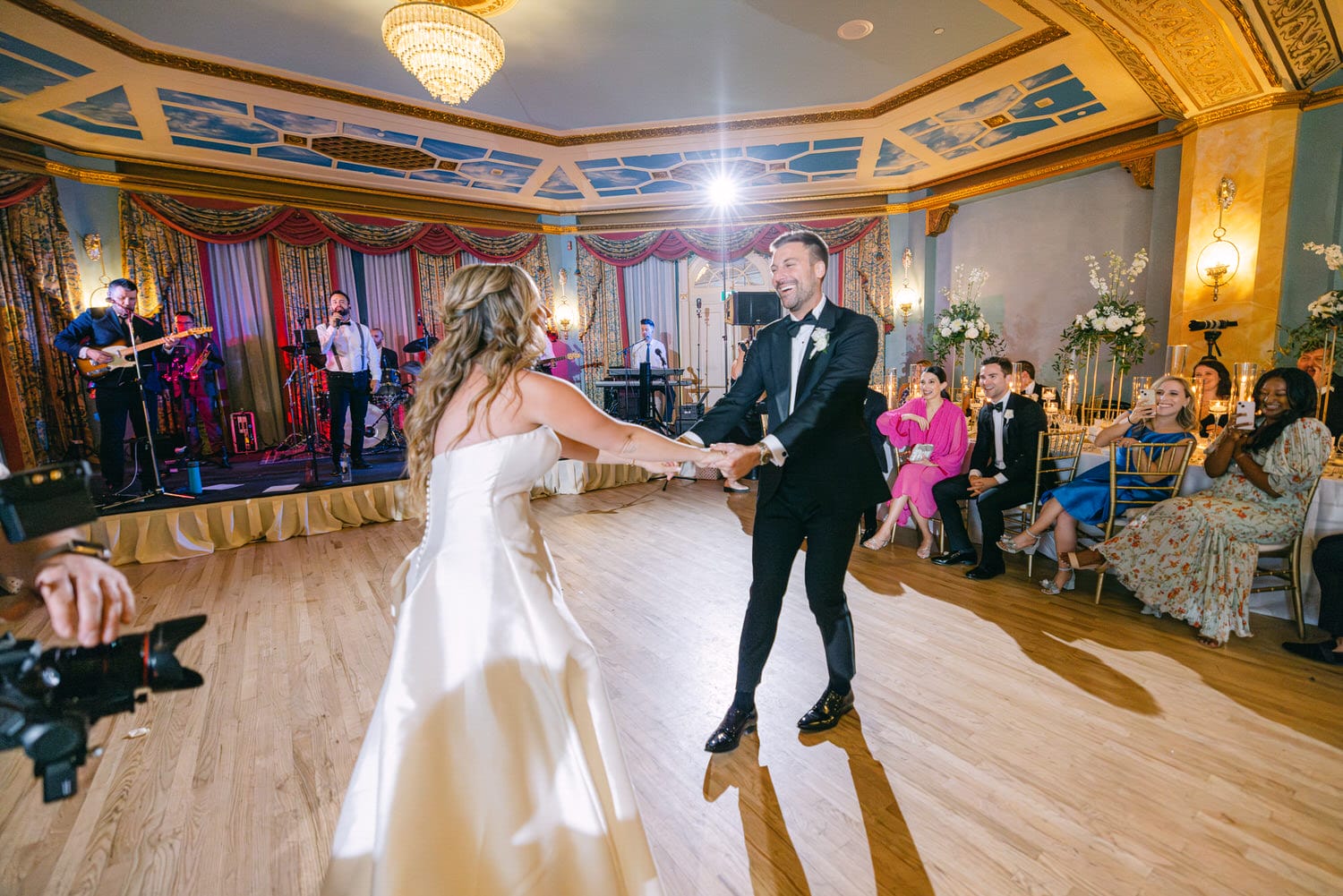 A couple joyfully dancing together at their wedding reception, surrounded by guests and a live band.