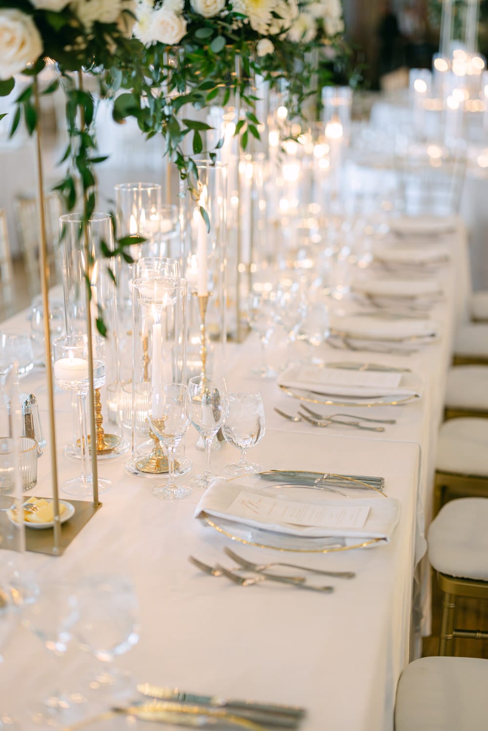 A beautifully arranged long dining table adorned with flowers, candles, and fine glassware, creating a romantic ambiance.