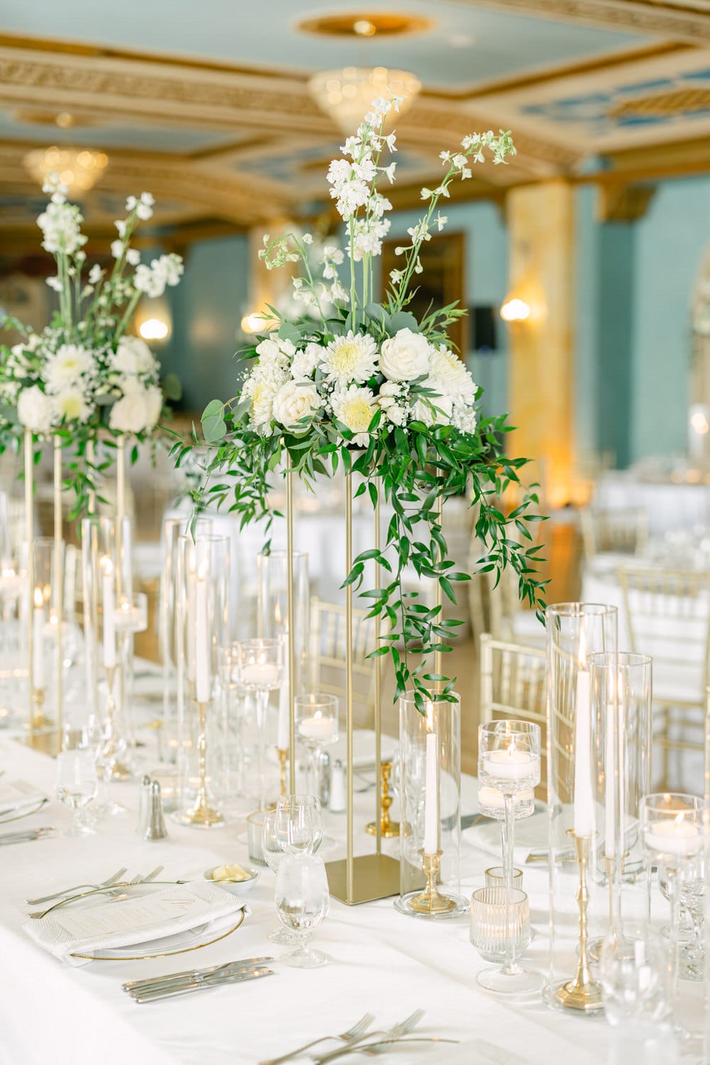 A beautifully arranged table setting with white floral centerpieces, candles, and fine dining accessories in an elegant venue.