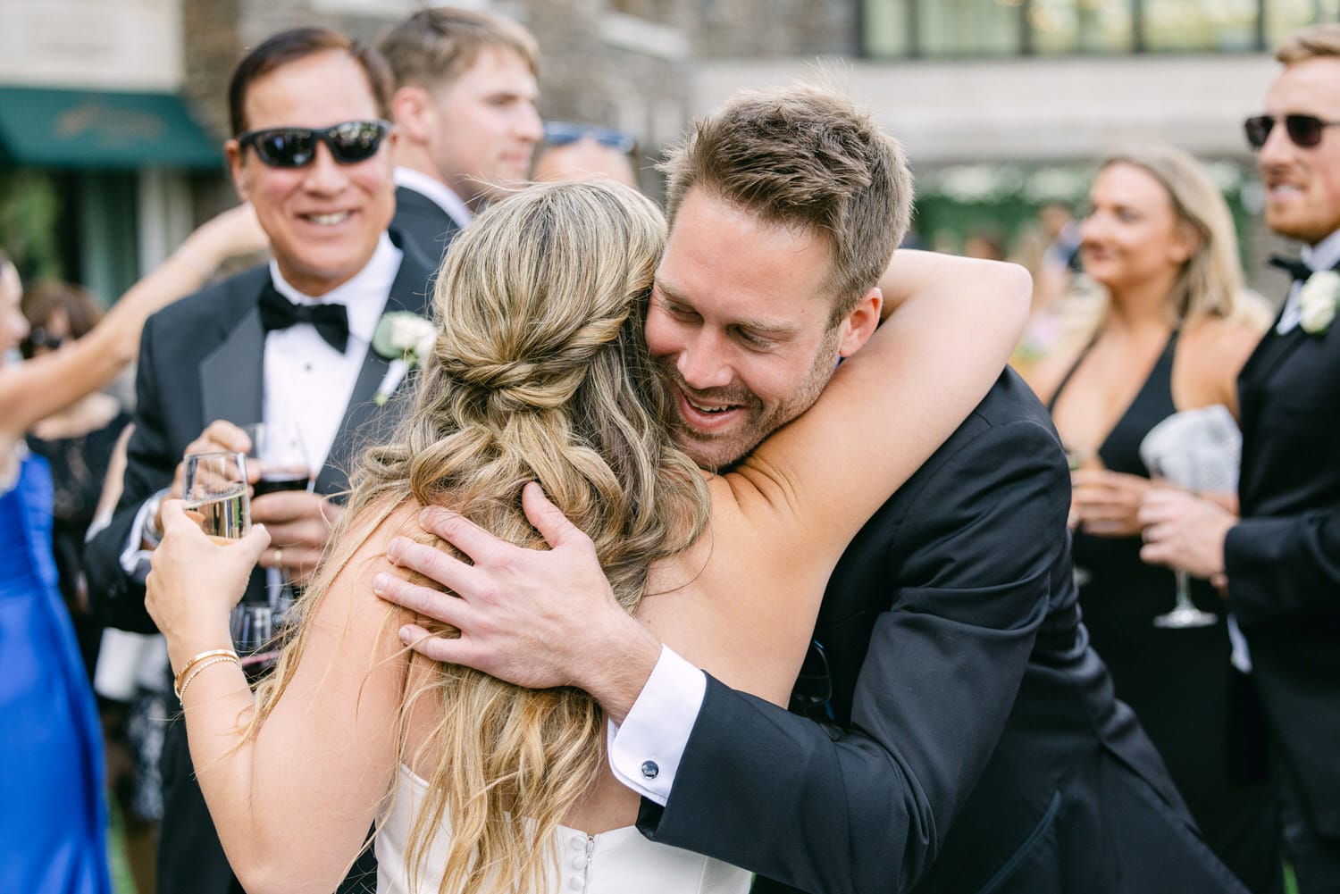 A joyful couple shares a warm embrace at a wedding reception, surrounded by other guests enjoying the festivities.