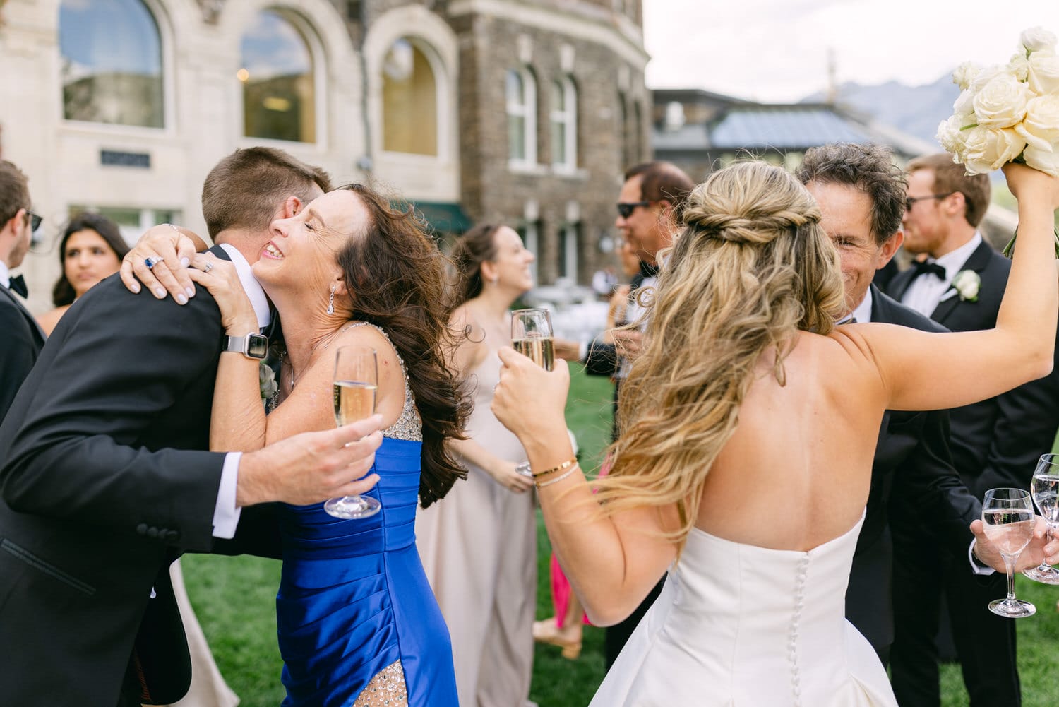 A joyful scene capturing guests embracing and toasting with champagne during a wedding reception outdoors, surrounded by elegant attire and smiles.