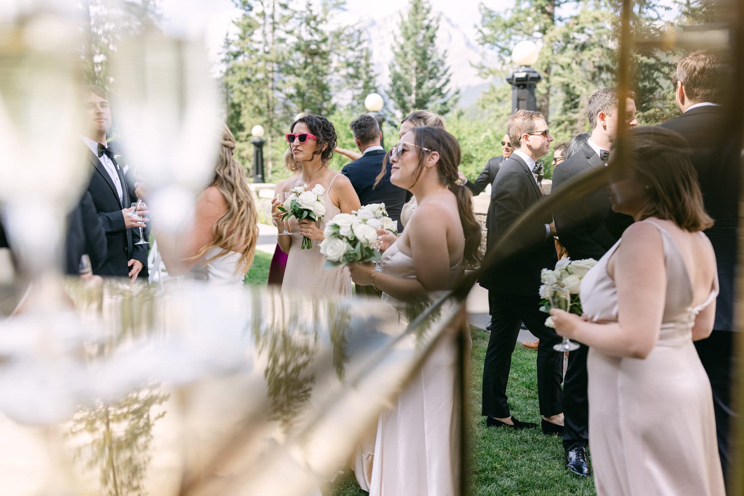 Guests mingling at a wedding reception, enjoying drinks and flowers, with a backdrop of lush greenery and mountains.