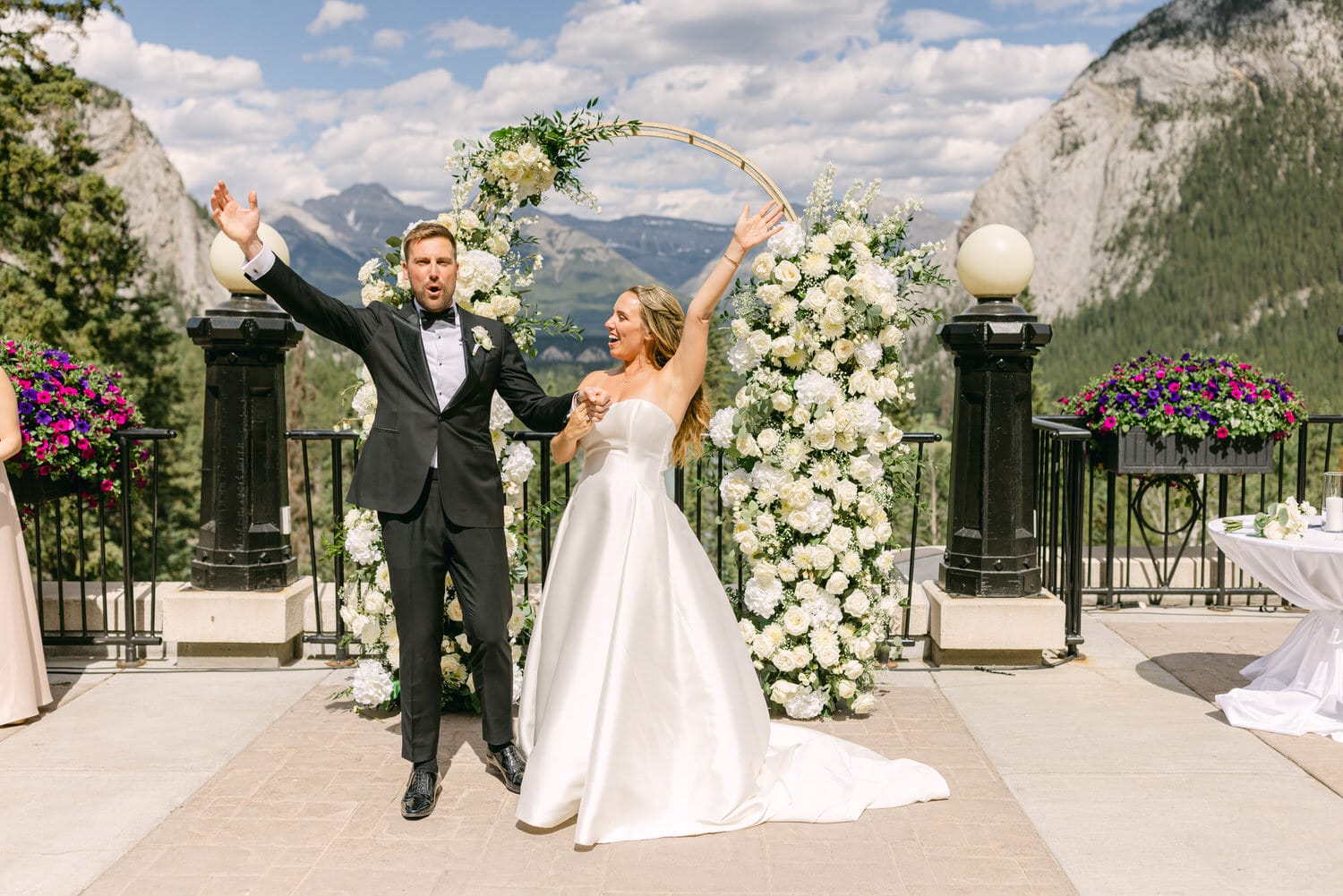 A joyful couple celebrates their wedding against a backdrop of mountains and floral decorations, capturing a moment of happiness and commitment.