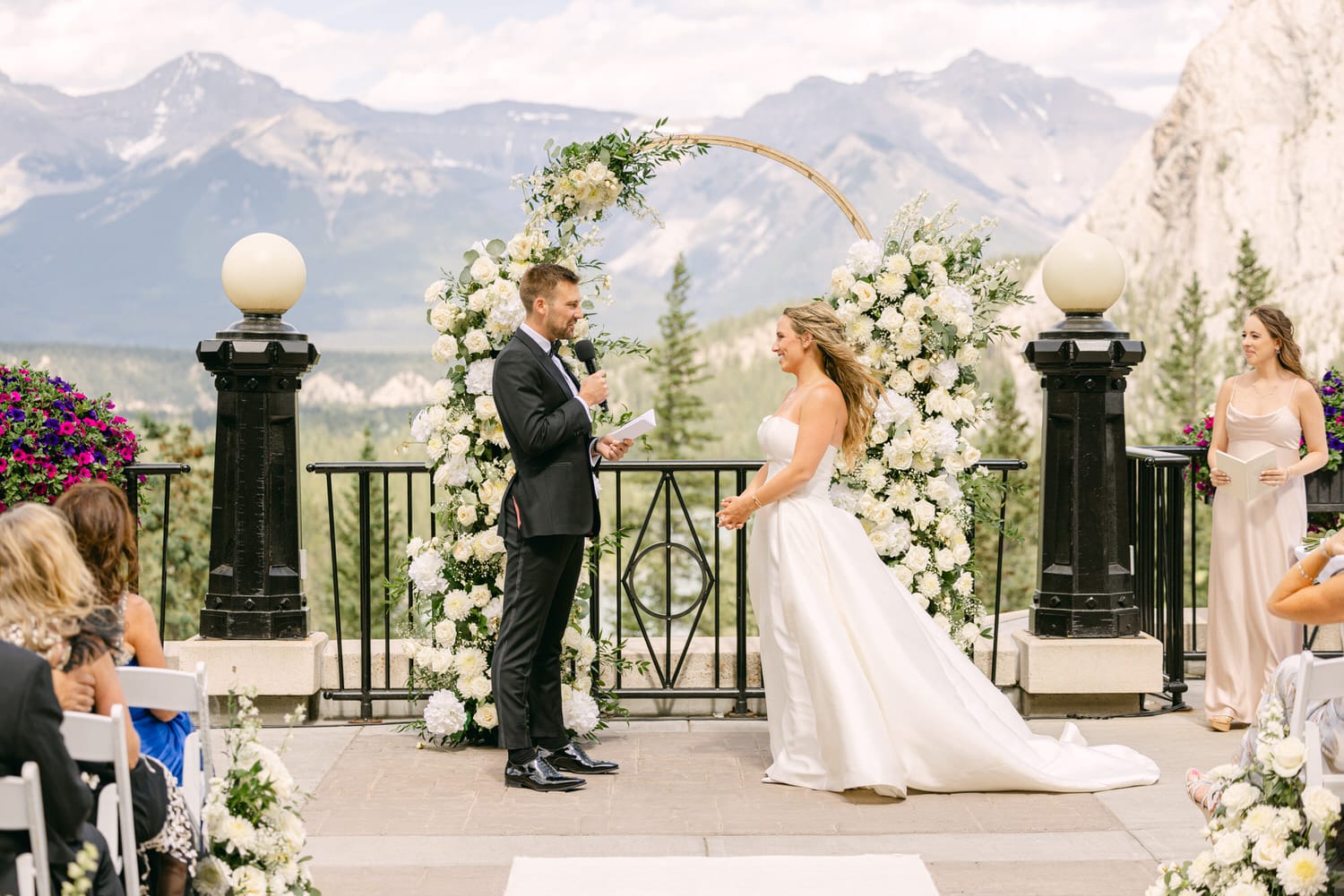 A couple exchanges vows at an outdoor wedding ceremony, surrounded by floral decorations and scenic mountain views.