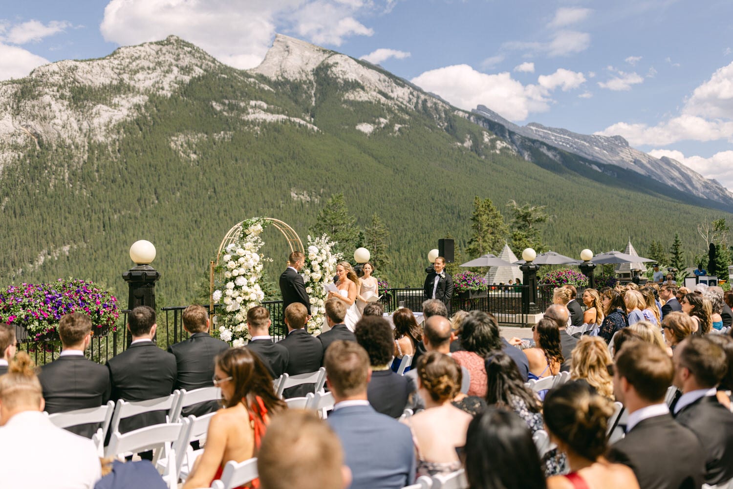 Guests seated at an outdoor wedding ceremony with a scenic mountain view and floral decorations.